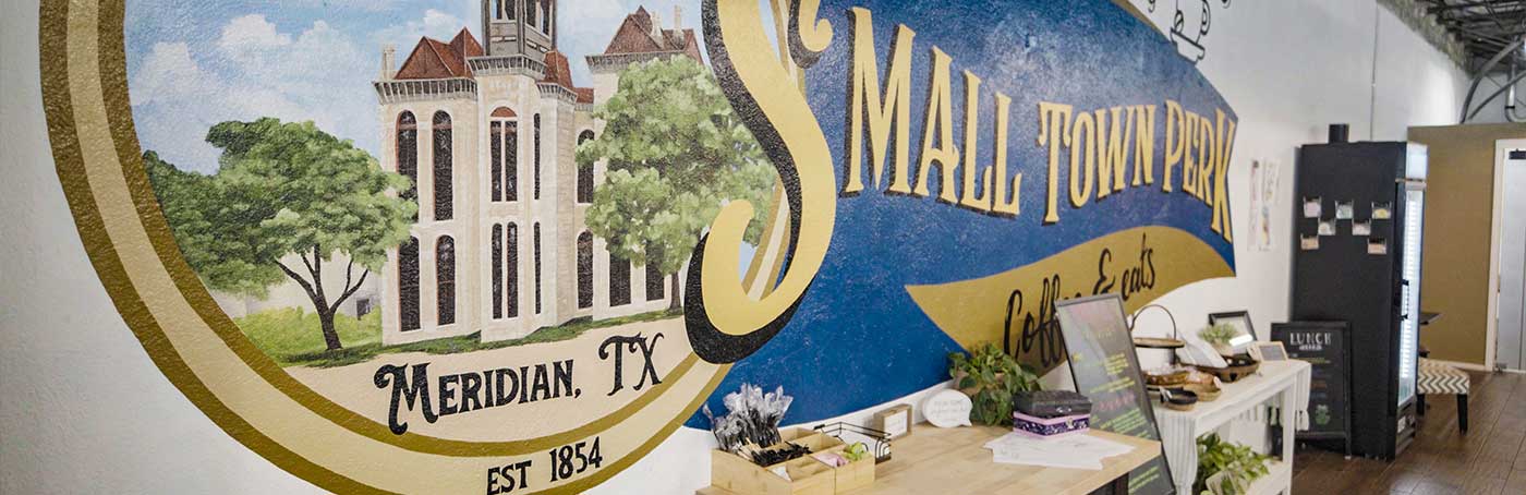 Mural on a wall depicting a historical building with trees and the name "SMALL TOWN PERK Coffee & Events,"