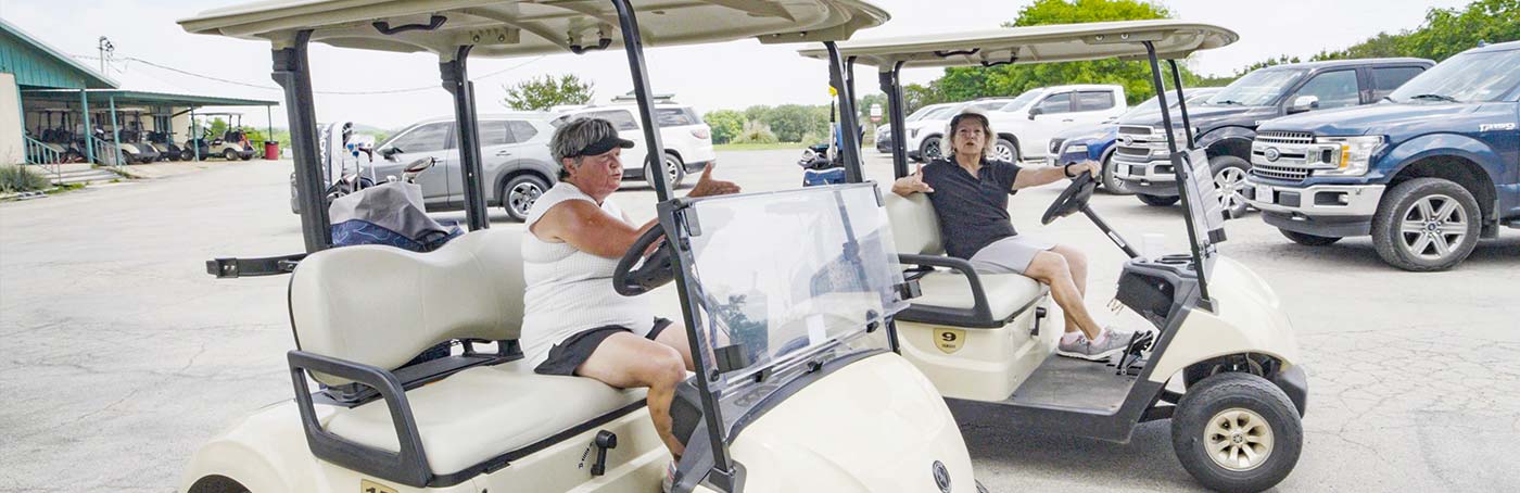 Two women in golf carts in a parking lot