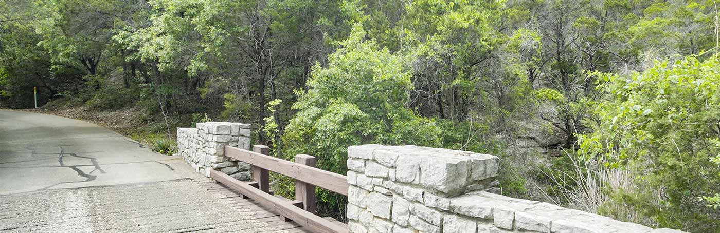 A stone bridge with wooden railings over a narrow road.