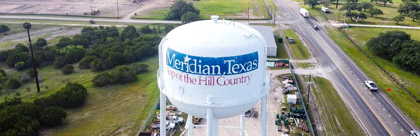 Water tower in Meridian, Texas, featuring blue and burgundy text reading "Meridian, Texas" and "Top of the Hill Country,"
