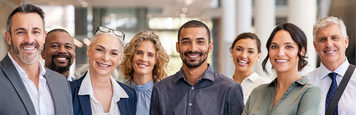 A close-up picture of a group of diverse men and women in business attire smiling at the camera