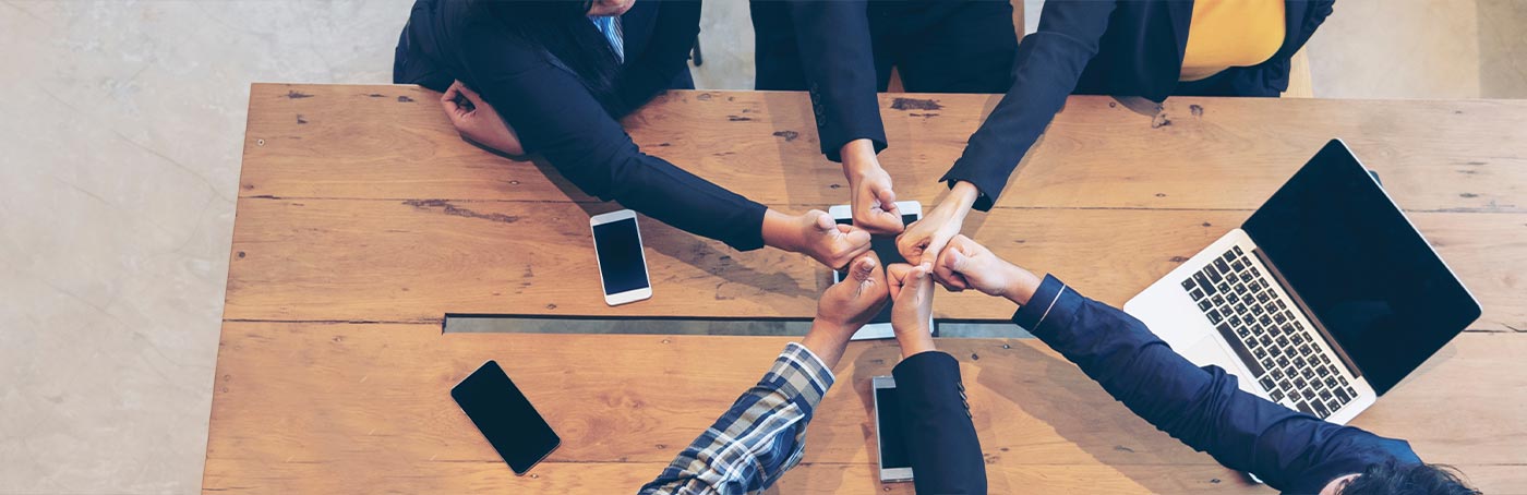 Close up of business men making thumbs up gesture together across a wooden table with a laptop