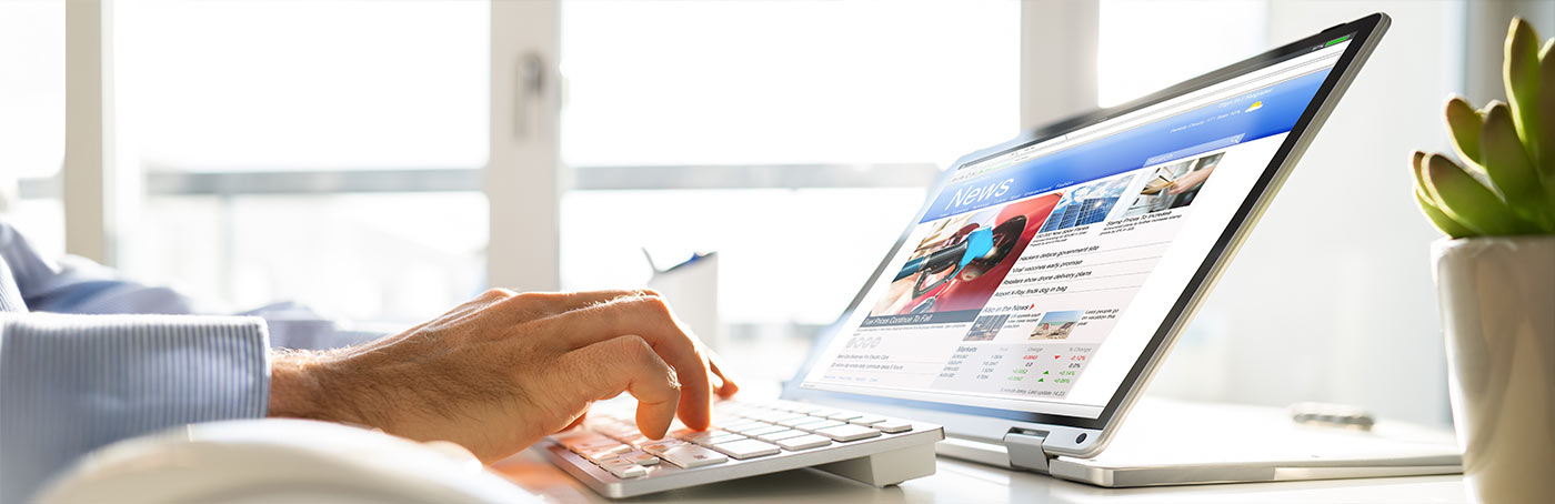 A man typing on a laptop with a news website up on the screen