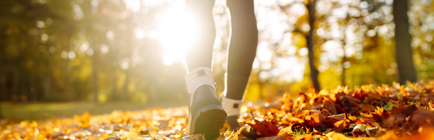 An image of a woman's boots, walking on a trail covered in Autumn leaves