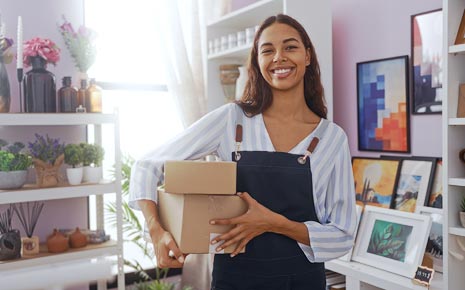 Woman with boxes smiles in front of an inventory of picture frames